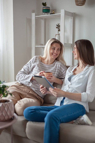 Two young women friends using tablet together, sitting on the couch, smiling and fun - Valokuva, kuva