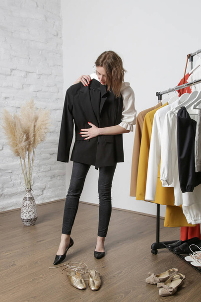 Mujer joven probándose una chaqueta negra en un taller de moda o un armario personal. - Foto, imagen