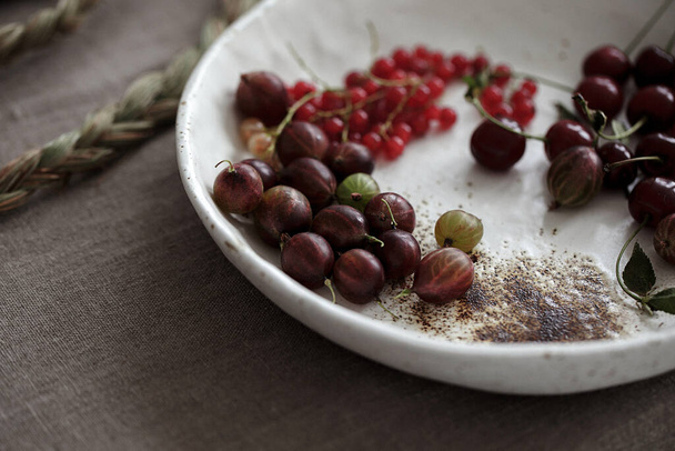 Craft white plate filled with gooseberries and red currants. Country rustic linen table set up - Fotografie, Obrázek