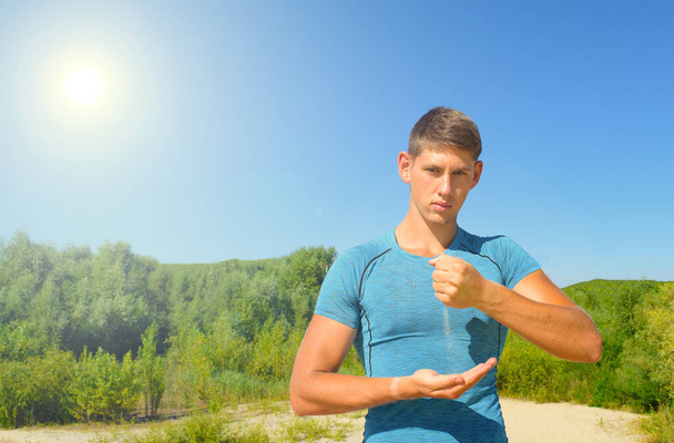 Junger Mann im blauen T-Shirt vor dem Hintergrund eines grünen Waldes und die Sonne scheint am Himmel - Foto, Bild