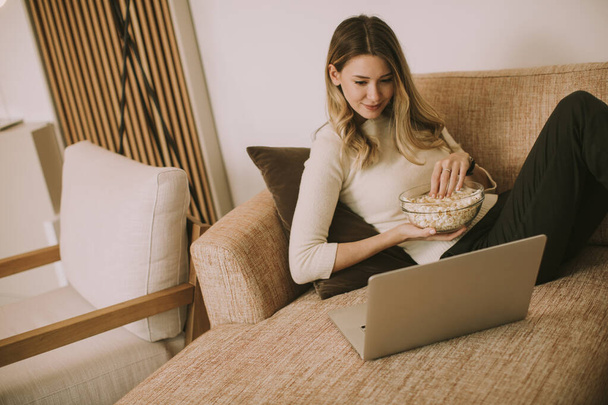 Молода красива жінка використовує ноутбук на дивані вдома
 - Фото, зображення