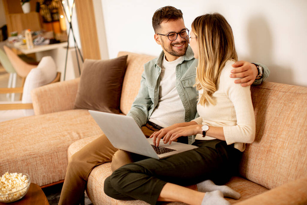 Hermosa pareja joven usando el ordenador portátil juntos mientras están sentados en el sofá en casa - Foto, imagen