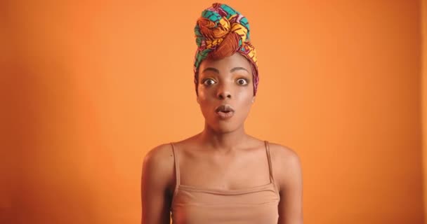 Chica negra sorprendida en el video. Mujer africana con turbante naranja sobre fondo naranja. - Metraje, vídeo