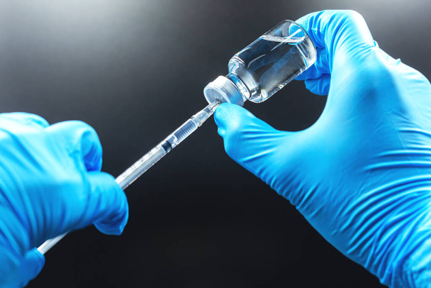 Het vaccinconcept is in handen van een medicijnflesje en een blauwe handschoen met kopieerruimte, geïsoleerd op zwarte achtergrond. - Foto, afbeelding