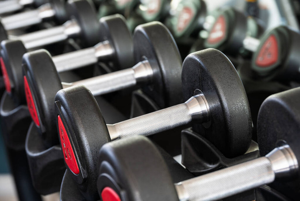 Row of metal dumbbells on rack in sports club for weight training - Fotoğraf, Görsel