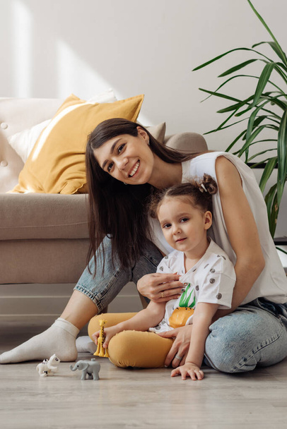 A dark-haired young mixed-race woman playing on the floor with her little daughter.Home interior design.Time together.Family concept and Mother's Day concept. - Photo, image