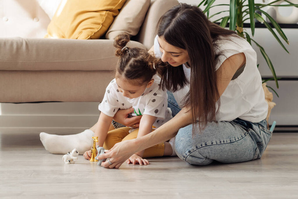 A dark-haired young mixed-race woman playing on the floor with her little daughter.Home interior design.Time together.Family concept and Mother's Day concept. - Foto, Imagem