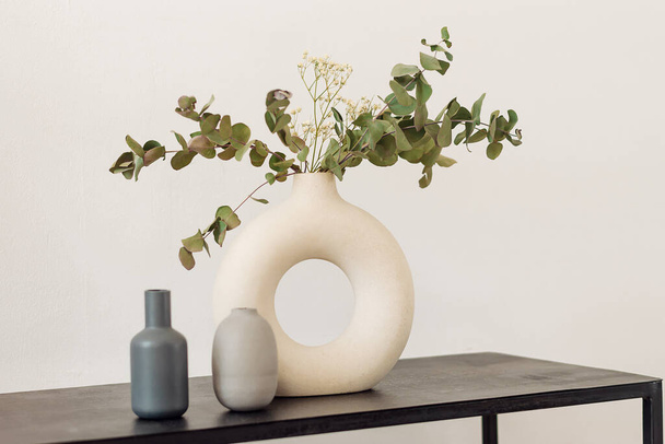 White creative stylish vase with eucalyptus branches and gypsophila on a black shelf.Interior design.Minimalistic style. - Photo, Image