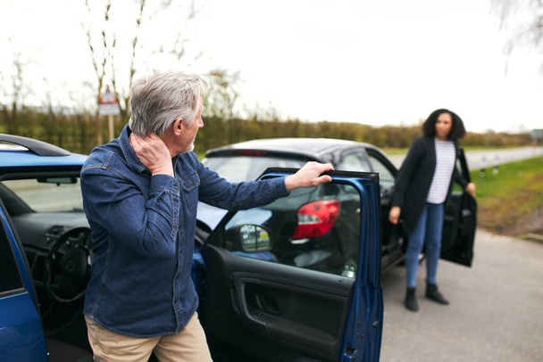 Los conductores mayores y las mujeres más jóvenes salen de los coches e inspeccionan los daños después de un accidente de tráfico - Foto, Imagen
