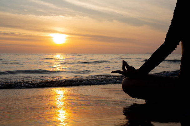 Силуэт женщина практикует йогу на пляже на закате. - Фото, изображение