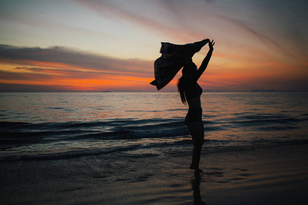 Силуэт женщины, стоящей на пляже на закате. - Фото, изображение