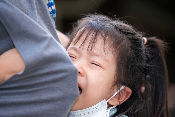 Miękkie skupienie. Słodkie azjatyckie dziecko płacze i żałuje, że zagnieździła się na brzuchu matki. Matka użyła ubrań, by otrzeć łzy na nieszczęśliwą dziewczynę. Dziecko głośno płacze. Urocze zażenowane dzieci w wieku 4 lat. - Zdjęcie, obraz