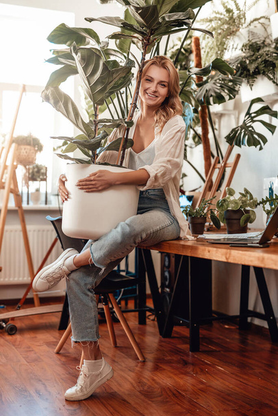 A pozitív női üzletember szobanövényekkel látja el az irodáját. - Fotó, kép