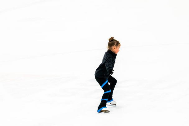 Petit patineur artistique en vêtements noirs pratiquant sur l'arène de glace intérieure. - Photo, image