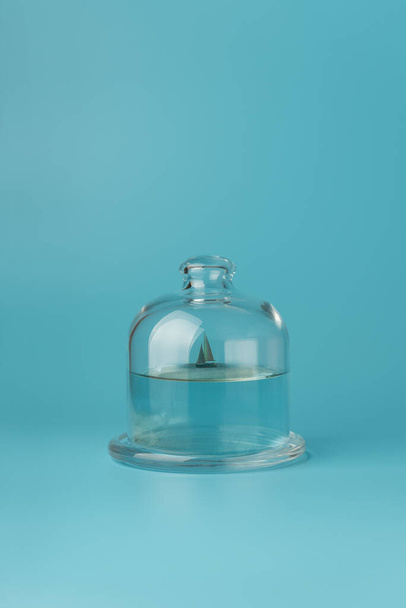 Glass cover dome with sailboat on blue background.  Creative summer vacation concept - 写真・画像