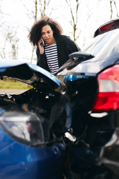 Mujer joven de pie junto a coche dañado después de accidente de tráfico reportar incidente a la compañía de seguros utilizando el teléfono móvil - Foto, Imagen