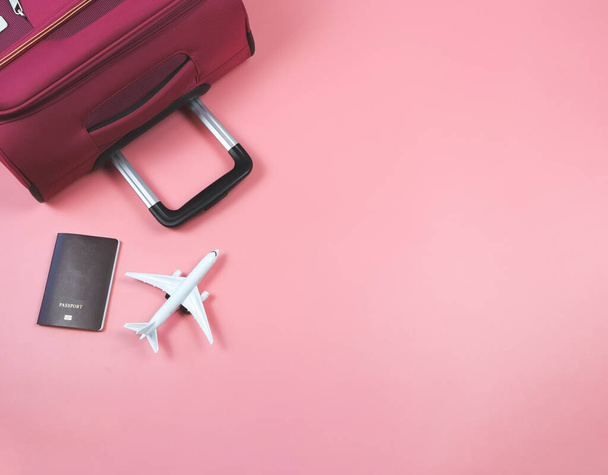 ピンクの背景に飛行機モデル、パスポート、ピンクのスーツケースのトップビューまたはフラットレイアウト。旅のコンセプト. - 写真・画像