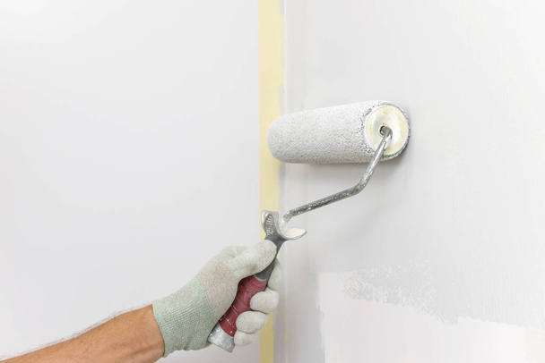 Un pintor está pintando una pared en una habitación con un rodillo. - Foto, Imagen