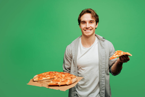 Nice man holds pizza and feel happy, isolated on green background - Photo, Image