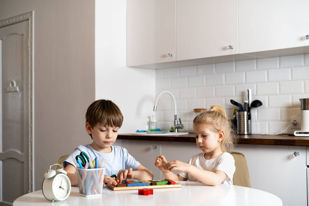boy and little girl at home in the kitchen, sit at a round white table and play board games, life at home.  - Foto, Bild