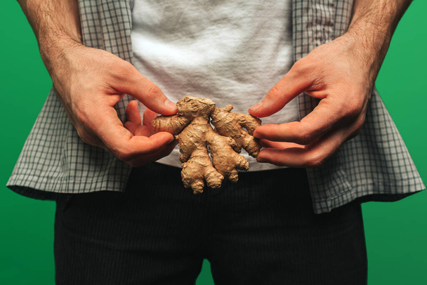 Close up young man holds ginger, isolated on green background - Photo, Image