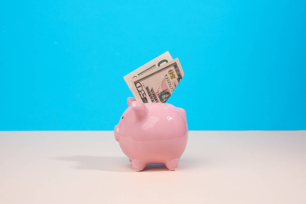 pink ceramic piggy bank with paper us dollars on a blue background. Money saving concept, keeping money in the bank - Foto, Imagen