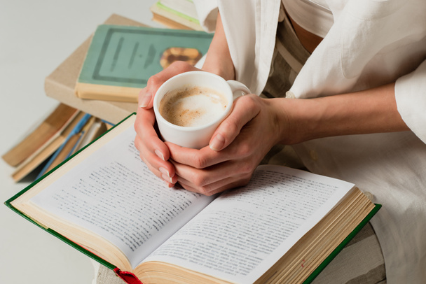 rajattu näkymä nainen kirjan tilalla kuppi kahvia eristetty valkoinen  - Valokuva, kuva