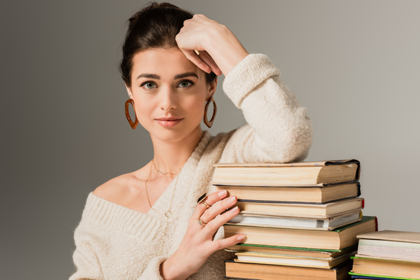 young woman in earrings leaning on stack of books on grey - Fotó, kép