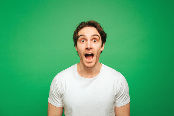 Young man looks surprised about news, isolated on green background - Foto, afbeelding