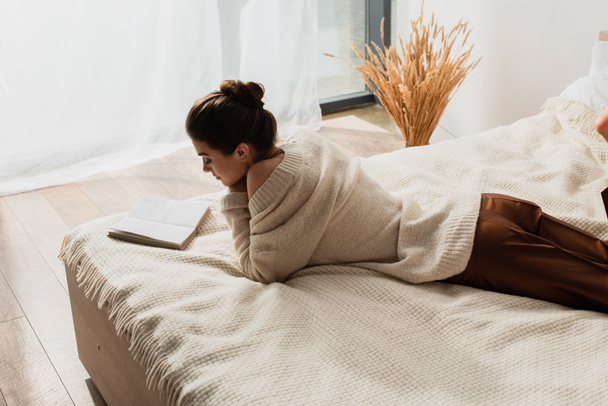 young woman reading book while resting on bed - Fotoğraf, Görsel