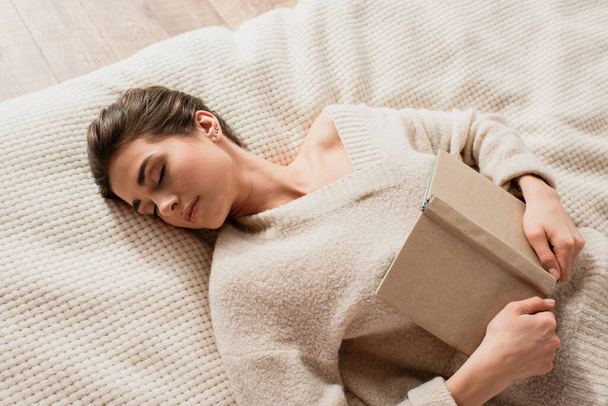 vista dall'alto della giovane donna che dorme con libro sul letto - Foto, immagini