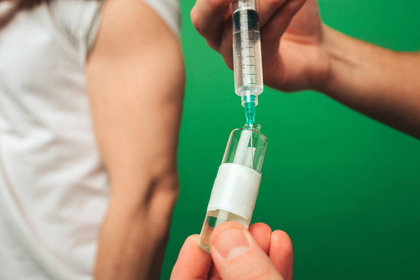 Close up syringe is drawn up liquid from an ampoule, isolated on green background - Photo, image