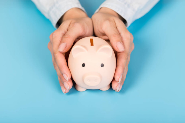 Piggy bank in hands on blue background, space for text. Finance, saving money - Fotó, kép