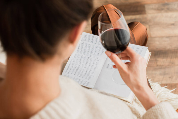 zamazana młoda kobieta czytająca książkę i trzymająca kieliszek czerwonego wina - Zdjęcie, obraz