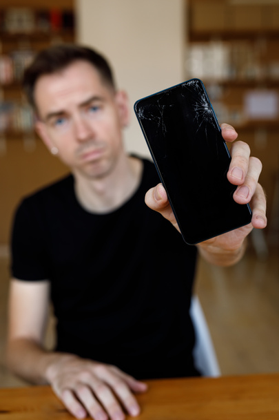 The sad man holds a broken smartphone with cracks - Photo, Image