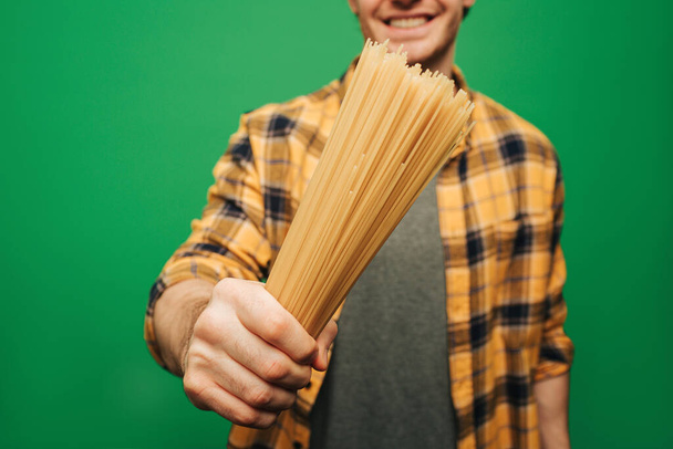 Giovane da vicino tiene gli spaghetti con il sorriso, isolato su sfondo verde - Foto, immagini