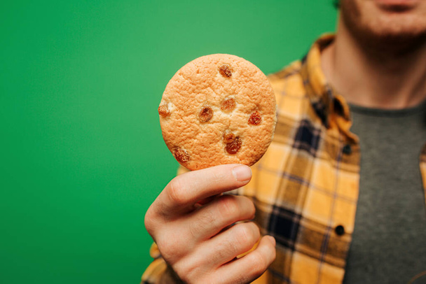 close-up jongeman houdt koekje, geïsoleerd op groene achtergrond - Foto, afbeelding
