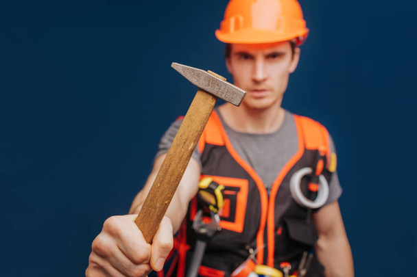Constructor de cerca en un casco con un martillo, aislado sobre fondo azul - Foto, imagen