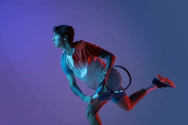 Young caucasian man playing tennis isolated on purple-blue studio background in neon, action and motion concept - Photo, image