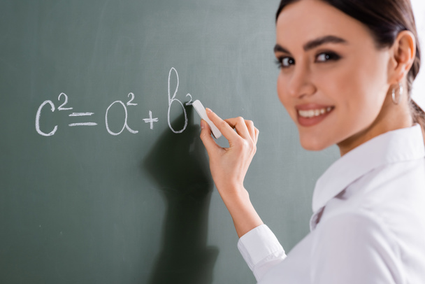 wazig leraar glimlachen op de camera tijdens het schrijven van wiskundige formule  - Foto, afbeelding