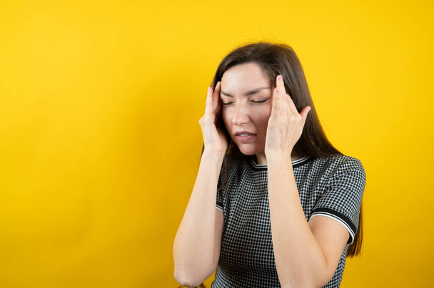 Porträt eines jungen Mädchens mit Kopfschmerzen auf gelbem Hintergrund.  - Foto, Bild