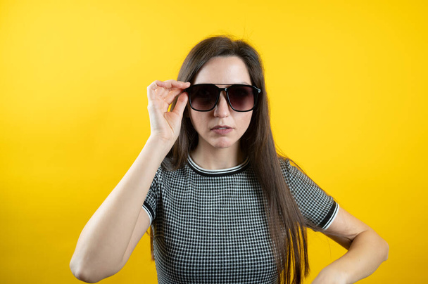 Porträt eines jungen Mädchens mit Sonnenbrille auf gelbem Hintergrund.  - Foto, Bild