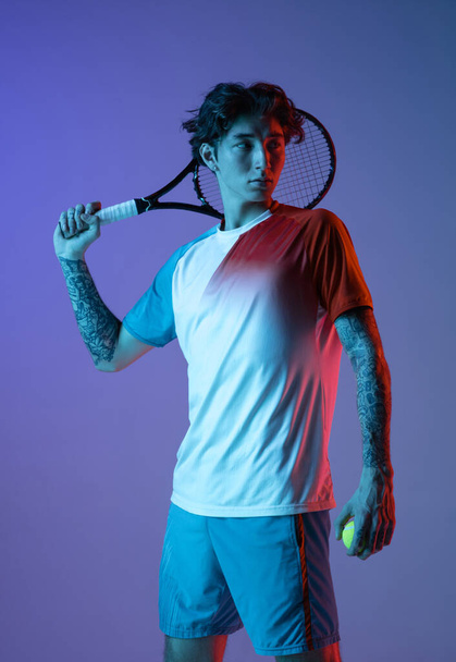 Young caucasian man playing tennis isolated on purple-blue studio background in neon, action and motion concept - Foto, Bild