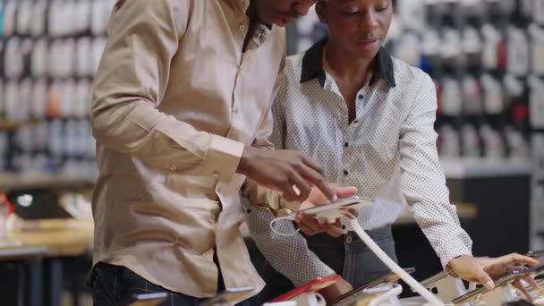 афро-американский мужчина и женщина делают покупки в магазине цифрового оборудования, покупатели обсуждают различные модели смартфонов - Кадры, видео