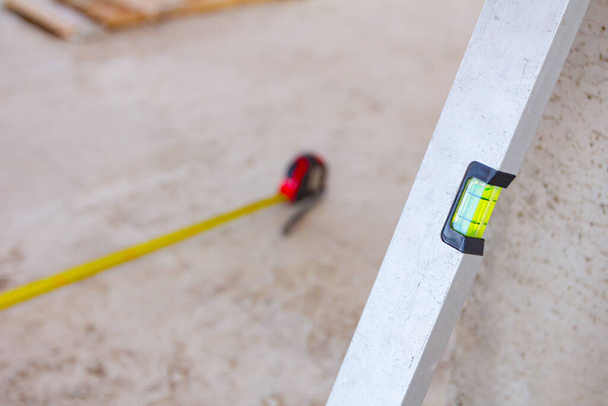 Spirit level placed next to the wall and metal measure tape is on the concrete floor after usage for construction site for measurement and control. - Valokuva, kuva
