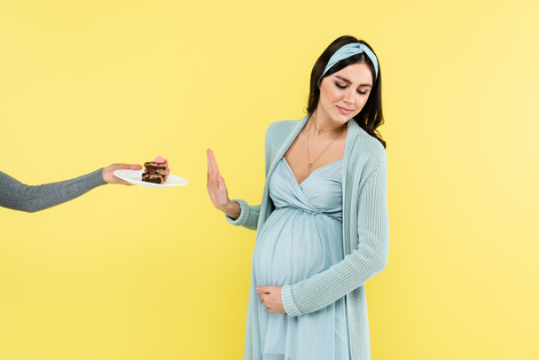 young pregnant woman showing reject gesture near sweet dessert isolated on yellow - Photo, Image