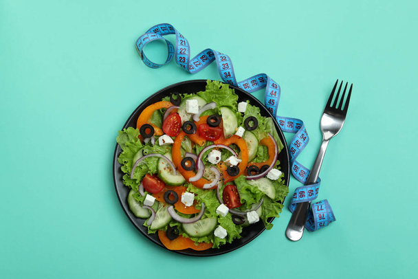 Plaat van Griekse salade, meetlint en vork op muntondergrond - Foto, afbeelding