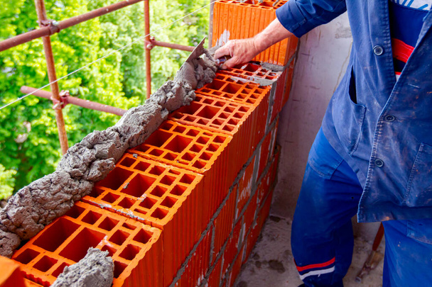 Robotnik używa szpachelki, kielni, do nanoszenia zaprawy na czerwone bloki do wykonania ściany, muru. - Zdjęcie, obraz