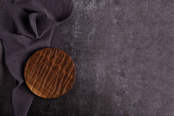 Empty vintage cutting board on dark background, food background concept. Round wooden board. Place under the label. Grey napkin - Photo, Image