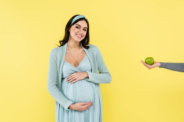 pleased woman touching belly near juicy apple isolated on yellow - Fotografie, Obrázek